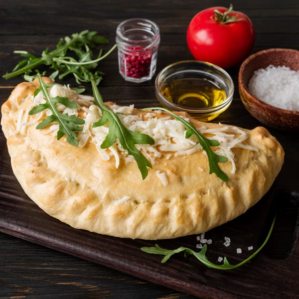 Gusto's Pizza calzone topped with shredded cheese and arugula, with olive oil, salt, and tomato.