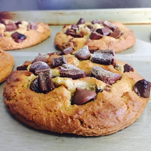 Freshly baked chocolate chip cookies with large chocolate chunks on a baking sheet.