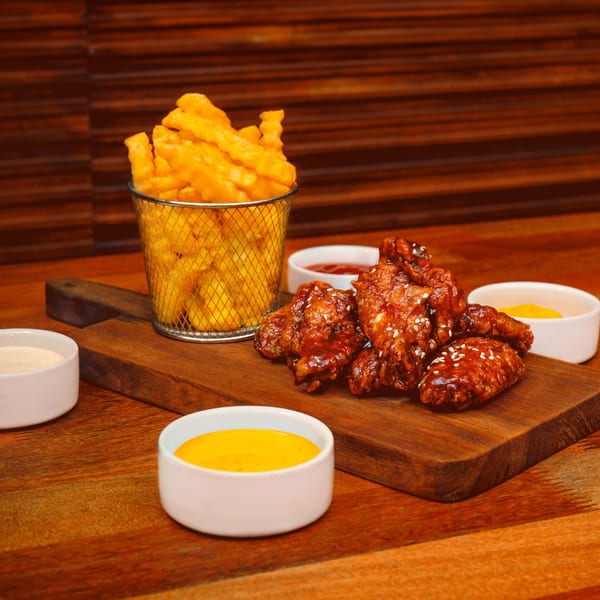 Gusto's Pizza's crispy french fries in a metal basket, with glazed chicken wings and dipping sauces.